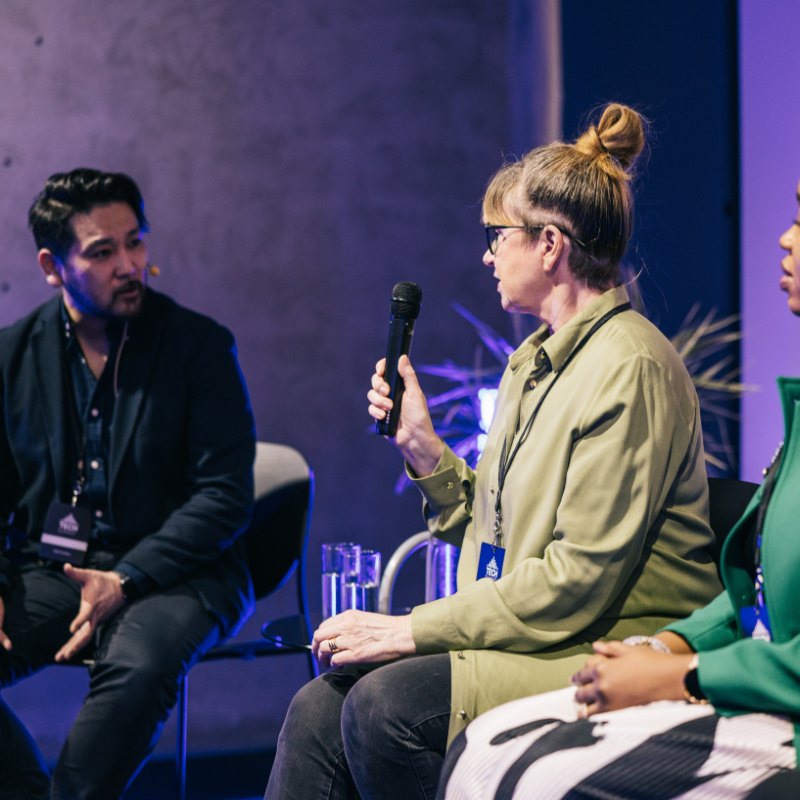 A panel in progress on stage, a speaker mid-answer with the microphone