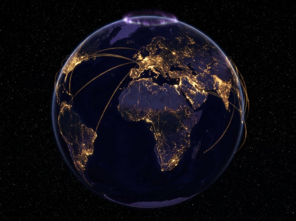 Earth at night from space, city networks glowing gold across several continents and joined by arcs of light
